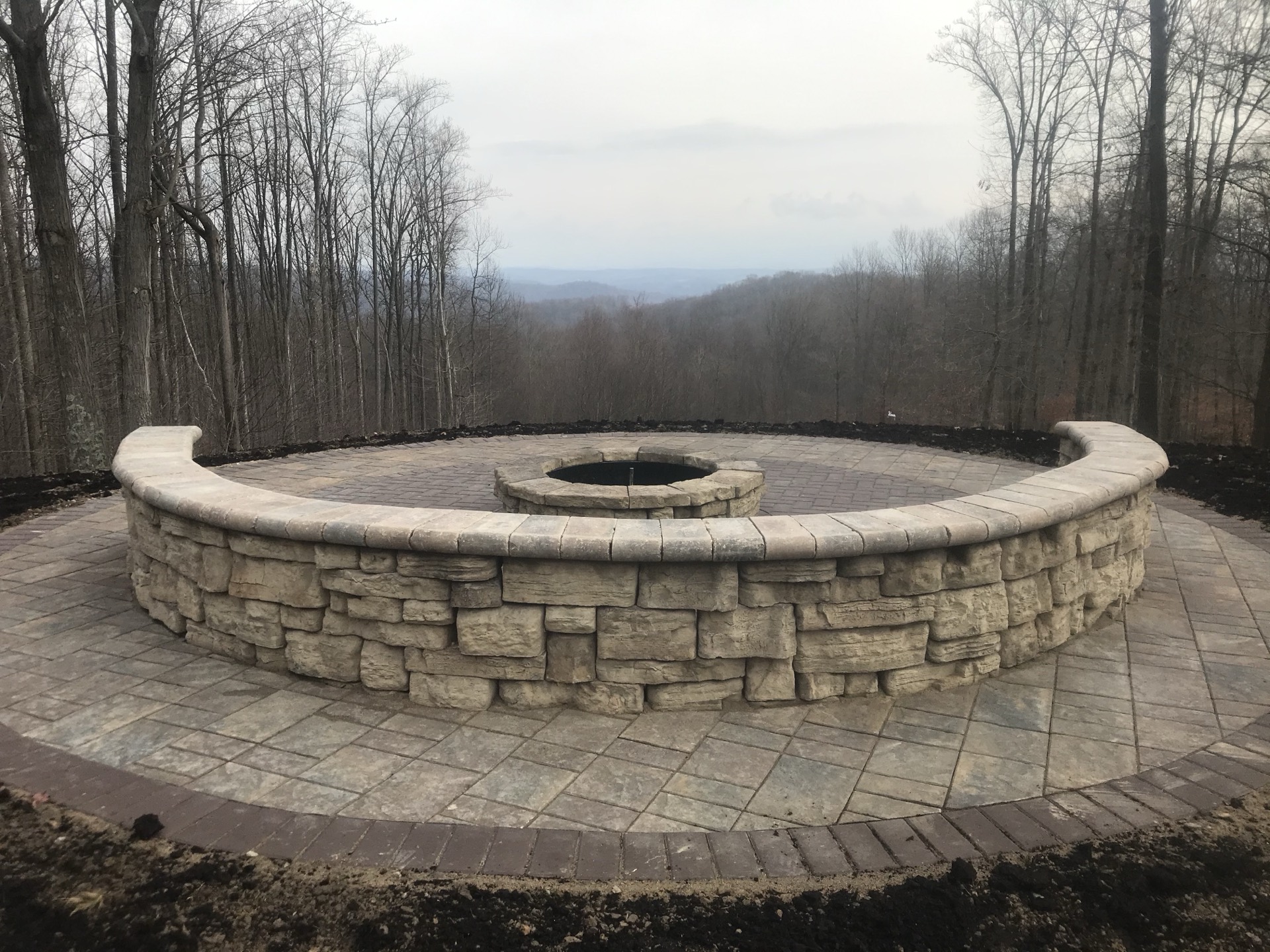 Stone firepit with a curved seating wall on a paver patio overlooking a mountain view
