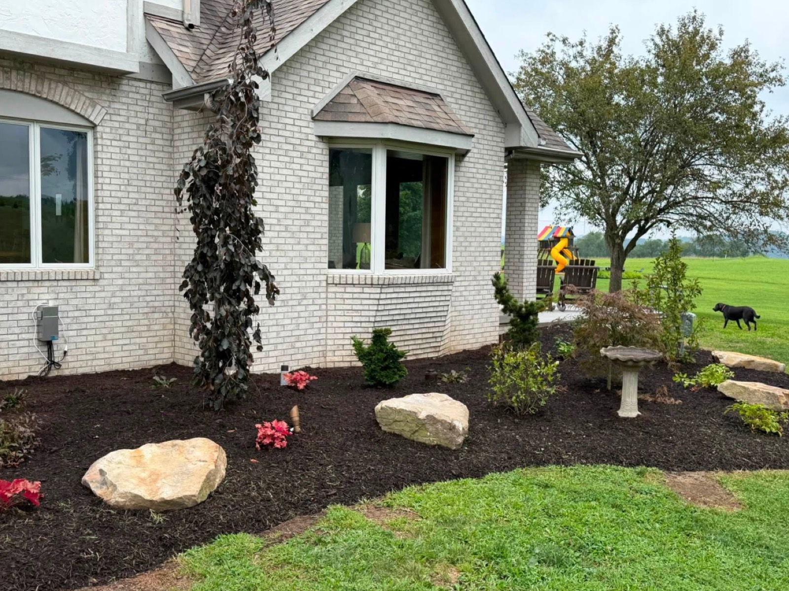 Fresh foundation plantings, mulch beds and boulders along a brick home