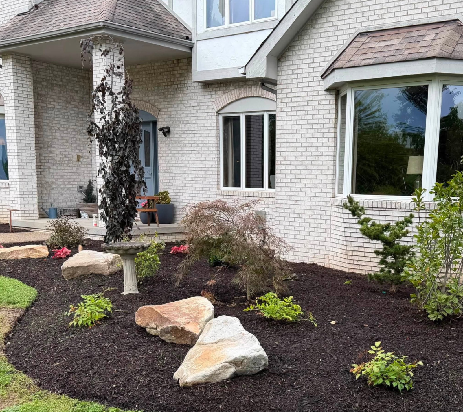 Front-yard landscape design with Japanese maple, boulders and a bench