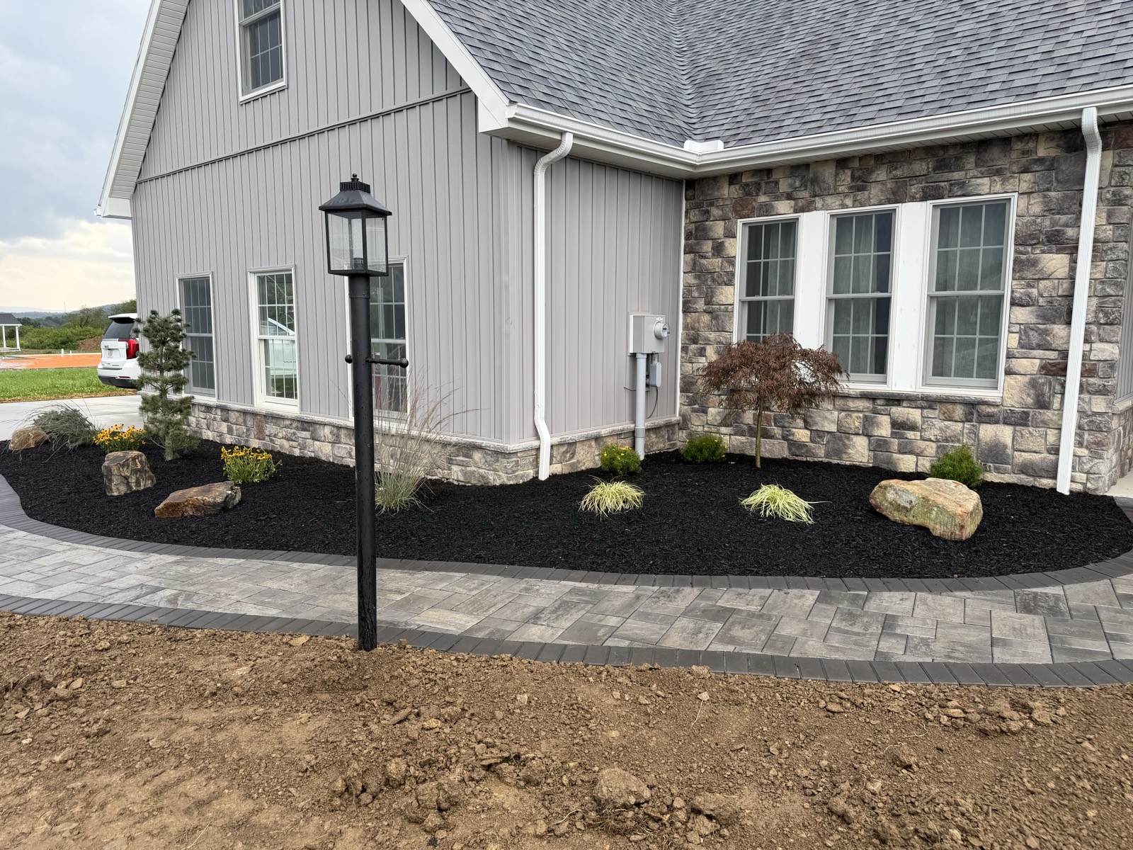 Landscape beds and boulders with a lamp post beside a paver walkway