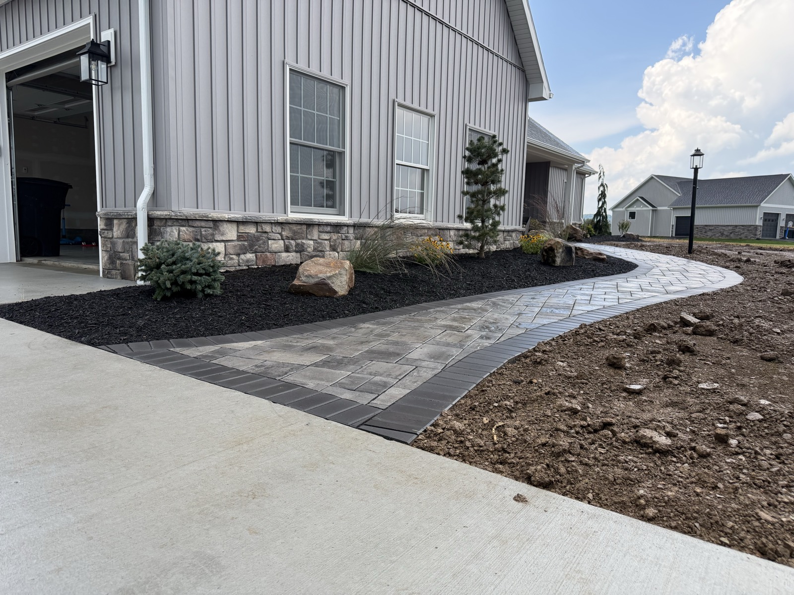 Curved paver walkway along a new-construction home with mulch beds